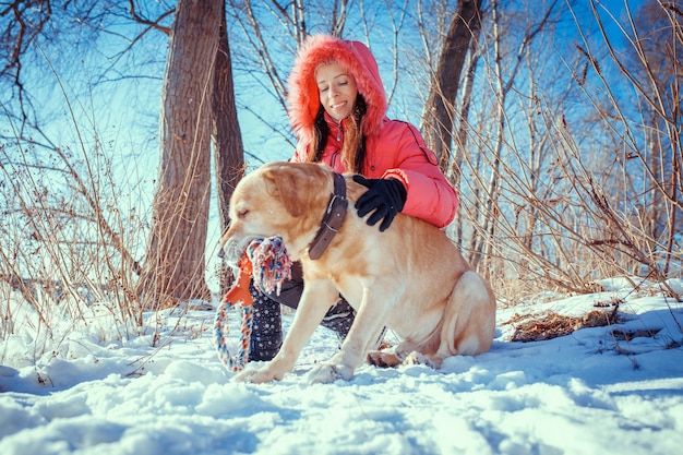 Meisje loopt met zijn gele labrador retriever in winterlandschap