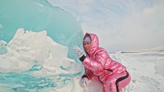 Meisje loopt op gebarsten ijs van het bevroren Baikalmeer Vrouw reiziger onderzoekt en kijkt naar een ijsschots Magische puurste plek in de natuur Ijs rond reiziger al zijn reis Wandelaar wandeling in kosmisch roze jasje