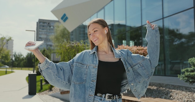 Meisje luistert naar muziek op de achtergrond van de stedelijke stad Gelukkige vrouw danst in het centrum erg emotioneel