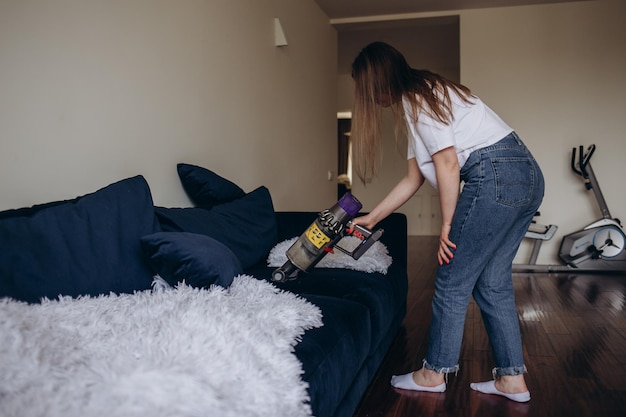 Meisje maakt de bank schoon met een stofzuiger