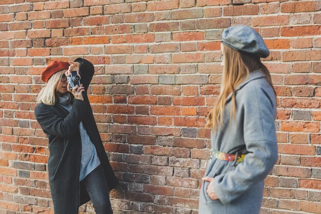 Meisje maakt foto van haar vriendin voor bakstenen muur in stadsstraatfotograaf en vinta