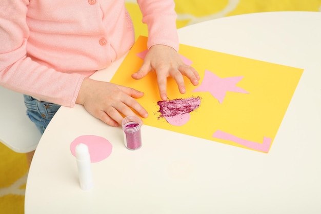 Meisje met behulp van kleurrijke glitter tijdens het maken van papieren kaart aan bureau in kamer close-up Thuiswerkplek