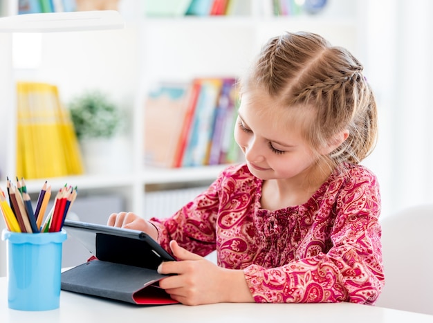 Meisje met behulp van tablet zittend op schoolbank in heldere klas