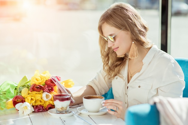 Meisje met bloemen, koffie, yoghurt en telefoon in een café