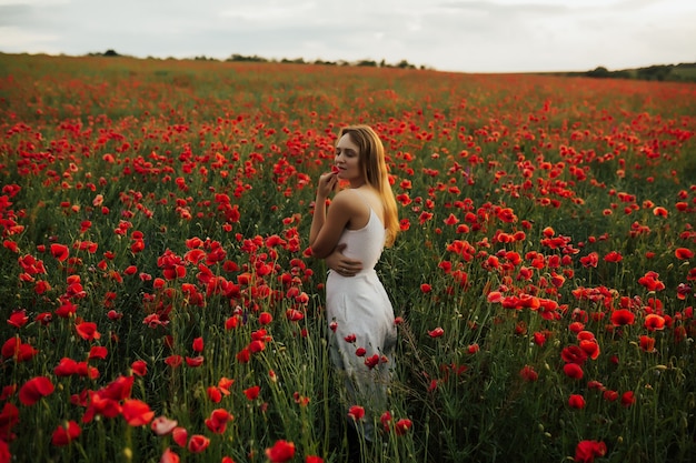 meisje met blond haar en witte jurk, staande in een veld met rode papavers