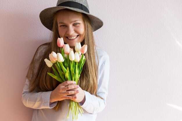 meisje met blond loshangend lang haar een vilten hoed op haar hoofd houdt lentebloemen in haar handen