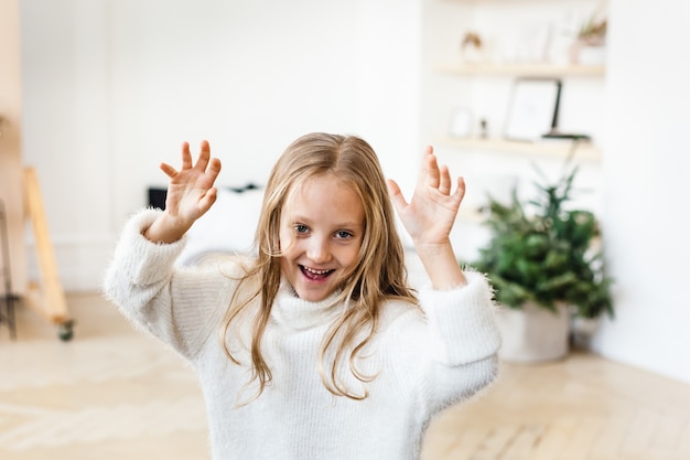 Meisje met blonde haren in een witte trui spelen in de buurt van de kerstboom, lachen, glimlachen,