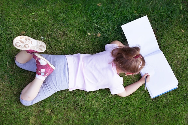 Meisje met bril ligt op het gras en tekent op papier