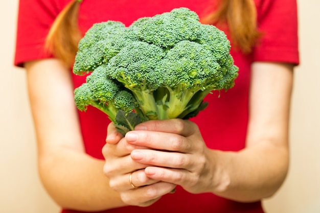 Meisje met broccoli in de hand op een rode achtergrond