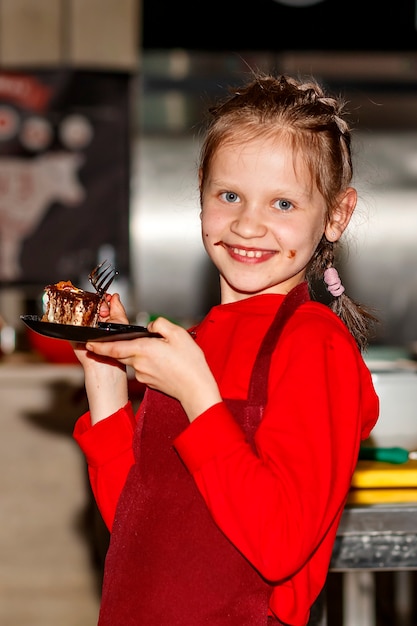 Meisje met chocolade op haar wangen houdt een bord cake vast en kijkt in de camera