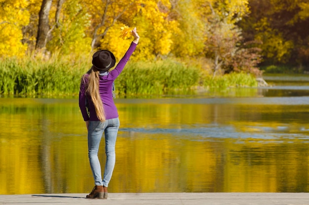 Meisje met de hoed staat op de pier met haar hand omhoog Herfst zonnig Achteraanzicht
