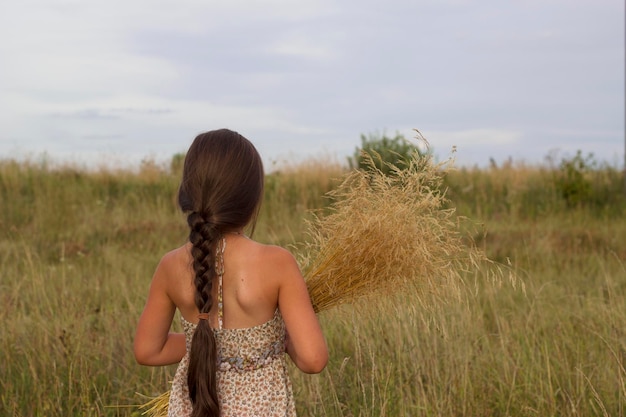 meisje met donker lang haar in zomerveld met boeket droog gras