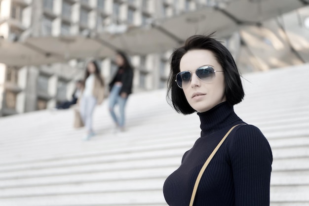 Meisje met donkerbruin haar in zwarte kleding. Vrouw in zonnebril op trappen. Mode en accessoire. Ambitie, uitdaging, succesconcept. Kijk, schoonheid, stijl. Parijse vrouw