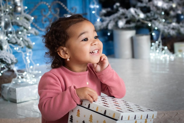 Meisje met donkere huidskleur ligt onder de kerstboom. schattige mulat viert het nieuwe jaar. Afrikaans meisje, geschenken