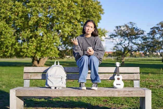 Meisje met droevig gezicht zittend op de bank met smartphone en ukelele die boos en teleurgesteld zijn