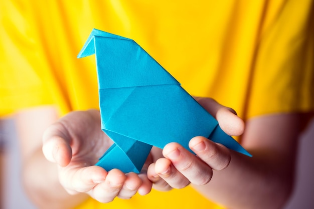 meisje met een blauwe origamivogel in haar handen op een gele achtergrond interessante hobby