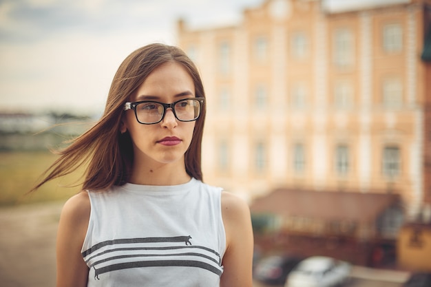 Meisje met een bril. stedelijk portret in de zomer op de achtergrond van gebouwen.