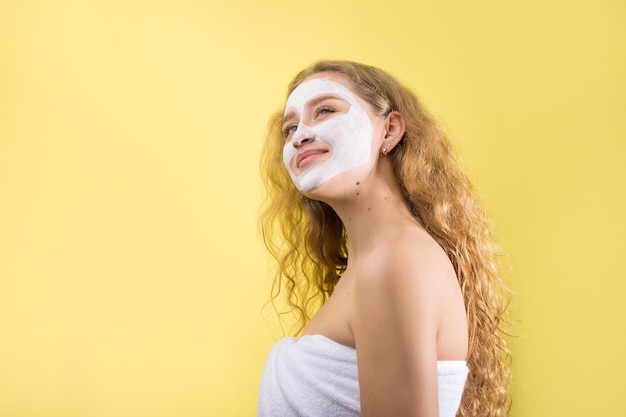 Meisje met een cosmetisch masker op haar gezicht in een witte handdoek