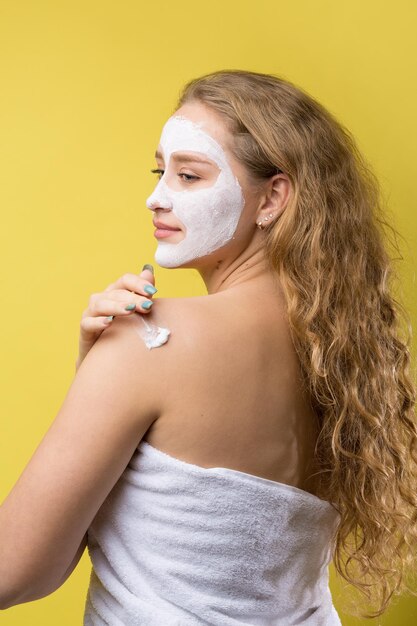 Meisje met een cosmetisch masker op haar gezicht in een witte handdoek.