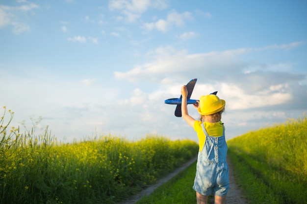 Meisje met een gele hoed lanceert een speelgoedvliegtuig in het veld, kijkt naar het pad. Zomertijd, kindertijd, dromen en onvoorzichtigheid. Luchtreis van een reisbureau op reis, avontuur en vakantie.