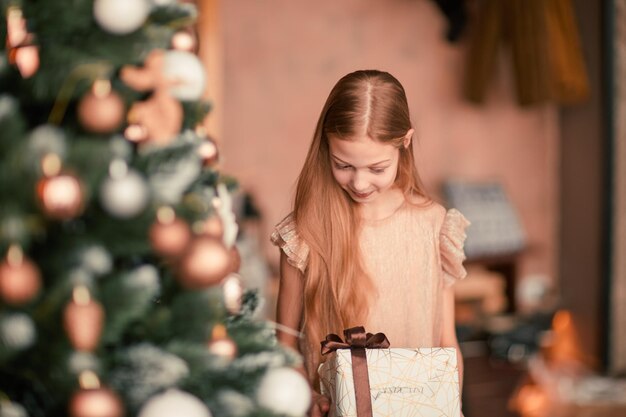 Meisje met een giftdoos die zich dichtbij de kerstboom bevindt