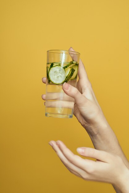 Meisje met een glas water met een komkommer op een gele studio als achtergrond