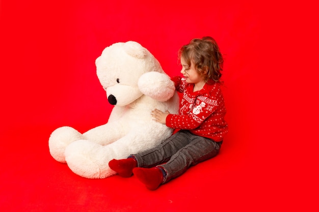 Meisje met een grote teddybeer in winterkleren op een rode achtergrond, ruimte voor tekst