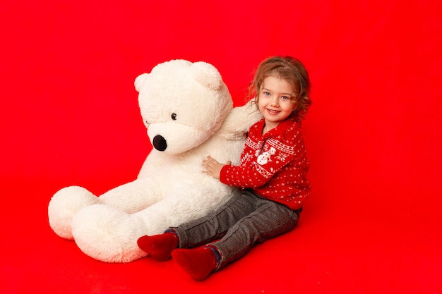 Meisje met een grote teddybeer in winterkleren op een rode achtergrond, ruimte voor tekst