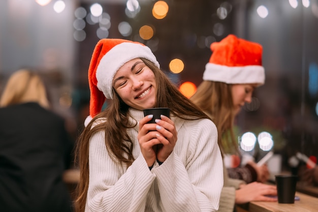 Meisje met een kerstmuts die in de coffeeshop zit en koffie drinkt