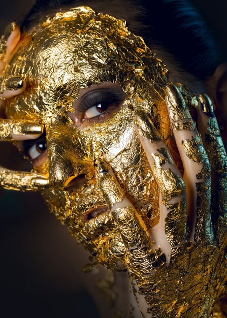 Meisje met een masker op haar gezicht gemaakt van bladgoud Somber studioportret van een brunette