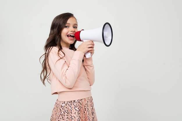 Meisje met een megafoon in hand zijdelings op een witte studiomuur met lege ruimte