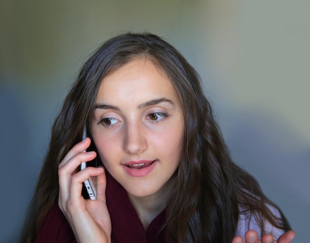 Meisje met een mobiele telefoon die op de grijze achtergrond spreekt.