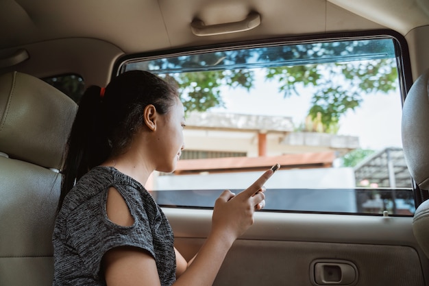 meisje met een mobiele telefoon zittend in de auto met het raam open tijdens het reizen