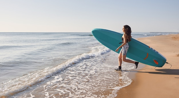 Meisje met een paddle-surfplank aan de kust van het strand kijkend naar de golven