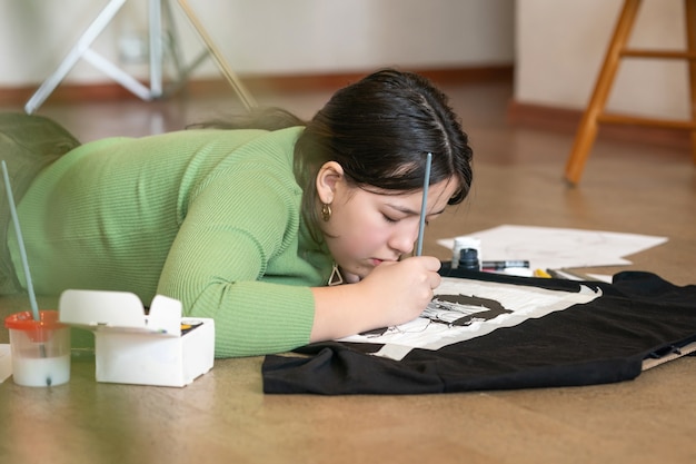 meisje met een penseel dat op kleren op de vloer van haar studio tekent