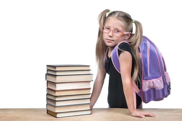 Meisje met een rugzak in een bril leunde tegen een houten tafel met een stapel boeken geïsoleerd op een witte achtergrond