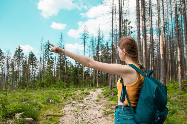 Meisje met een rugzak schudt zijn hand aan de zijkant, wandelen in het bos, geniet van de prachtige heuvels op een zonnige dag.