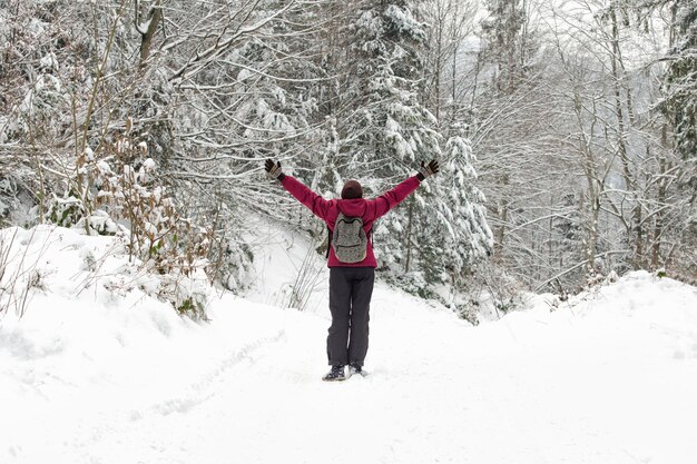 Meisje met een rugzak staat met opgeheven armen in een besneeuwd bos Winterdag