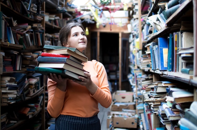 Meisje met een stapel boeken in de bibliotheek