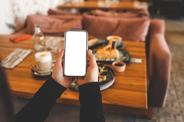 Meisje met een telefoon met een leeg scherm in een café met eten op de achtergrond