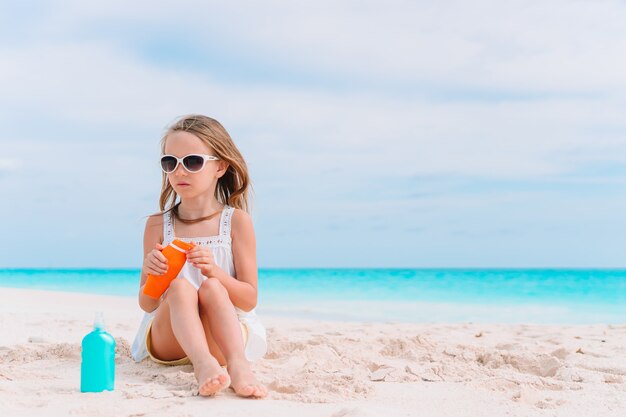 Meisje met fles zonnecrème zitten op tropisch strand