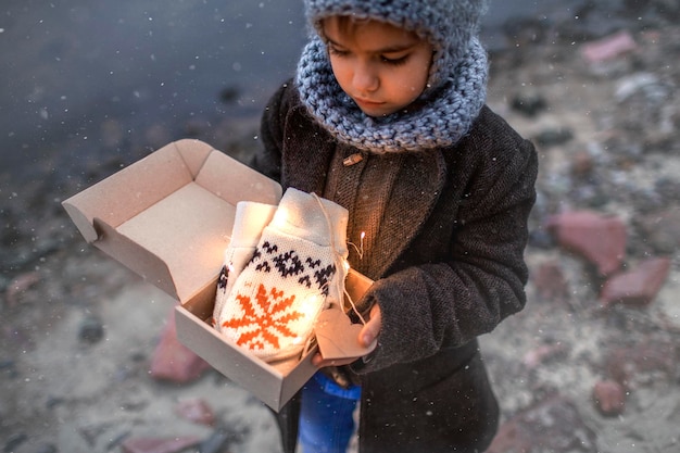 Meisje met gebreide grijze muts die een geschenkdoos opent met warme handschoenen