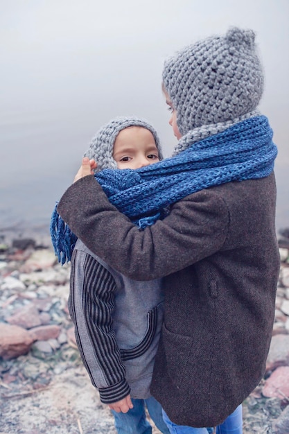 Meisje met gebreide grijze muts knuffelt haar bevroren kleinere broer een sjaal voor twee om warm te blijven