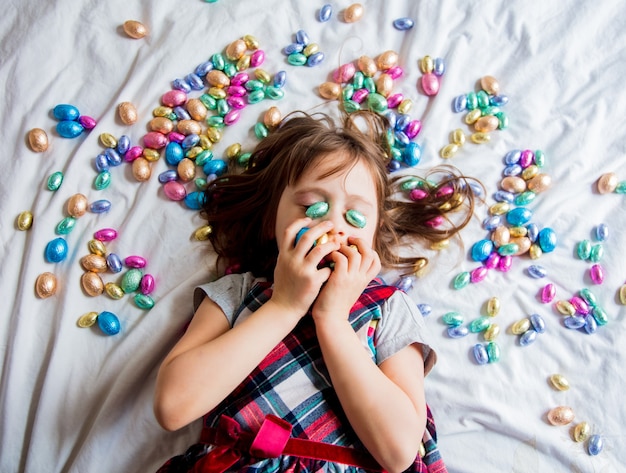 Meisje met gekleurde chocoladepaaseieren in een bed. Boven weergave.