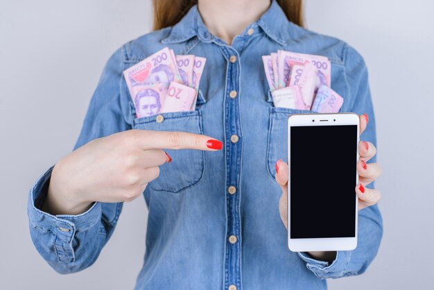 Meisje met geld in zakken wijst vinger op smartphone