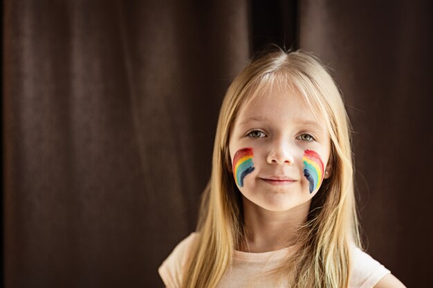 Meisje met geschilderde regenboog op gezicht tijdens quarantaine Covid-19