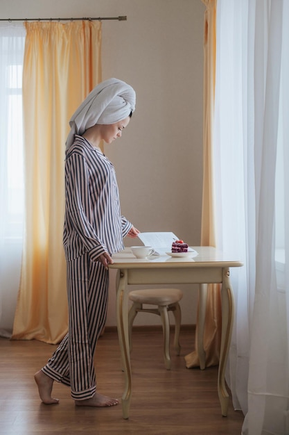 Meisje met haar gewikkeld in een handdoek en in pyjama die het boek op tafel leest met een stuk