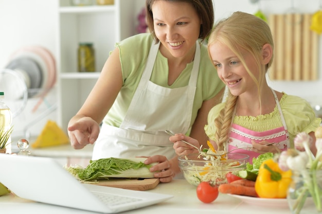 Meisje met haar moeder koken en kijken naar laptop