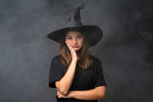 Meisje met heksenkostuum voor Halloween-partijen over geïsoleerde donkere muur ongelukkig en gefrustreerd