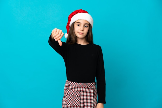 Meisje met kerstmuts geïsoleerd op blauwe achtergrond met duim omlaag met negatieve uitdrukking